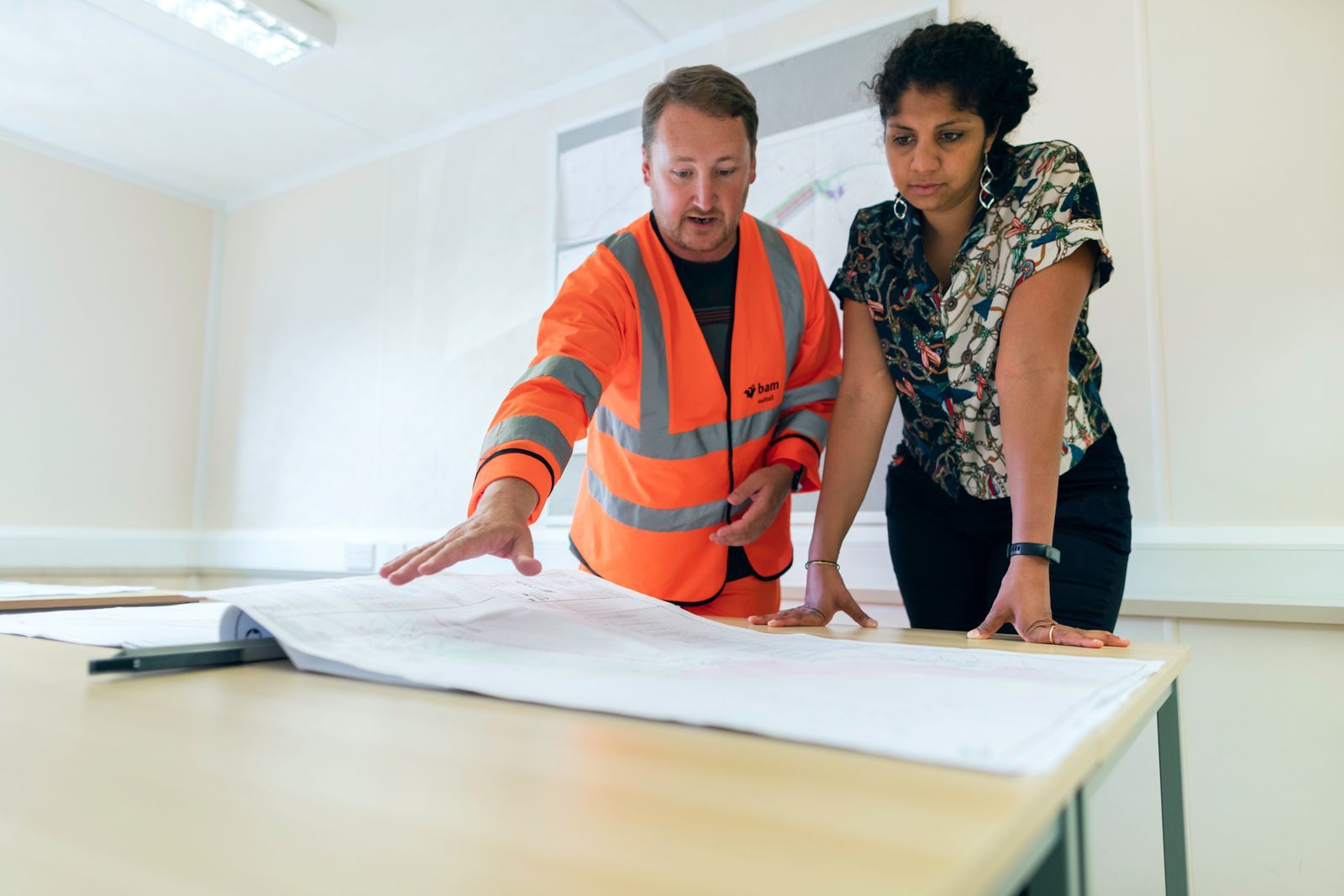 Two engineers reviewing blueprints in an office, discussing project details